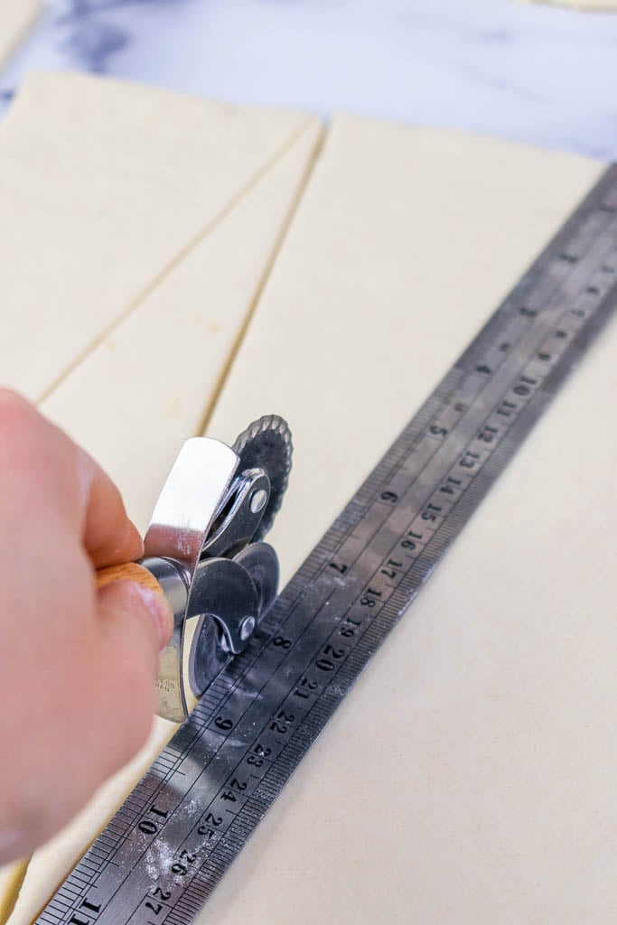 Cutting croissant triangles with a pastry wheel and using a ruler as a guide
