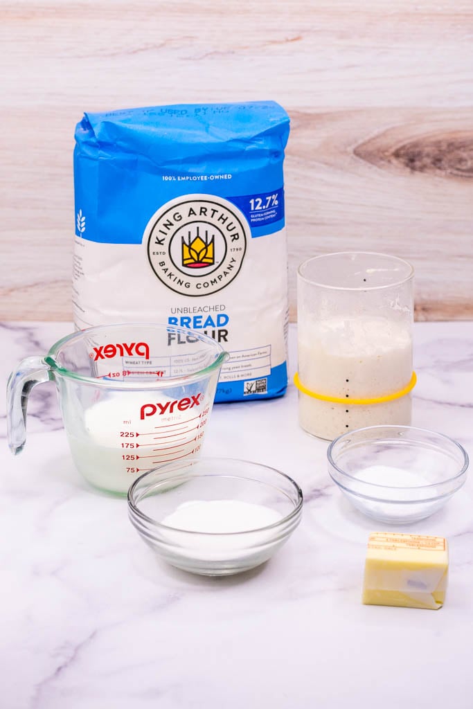 Ingredients needed for sourdough croissants including bread flour, milk, sugar, salt, sourdough starter, and butter