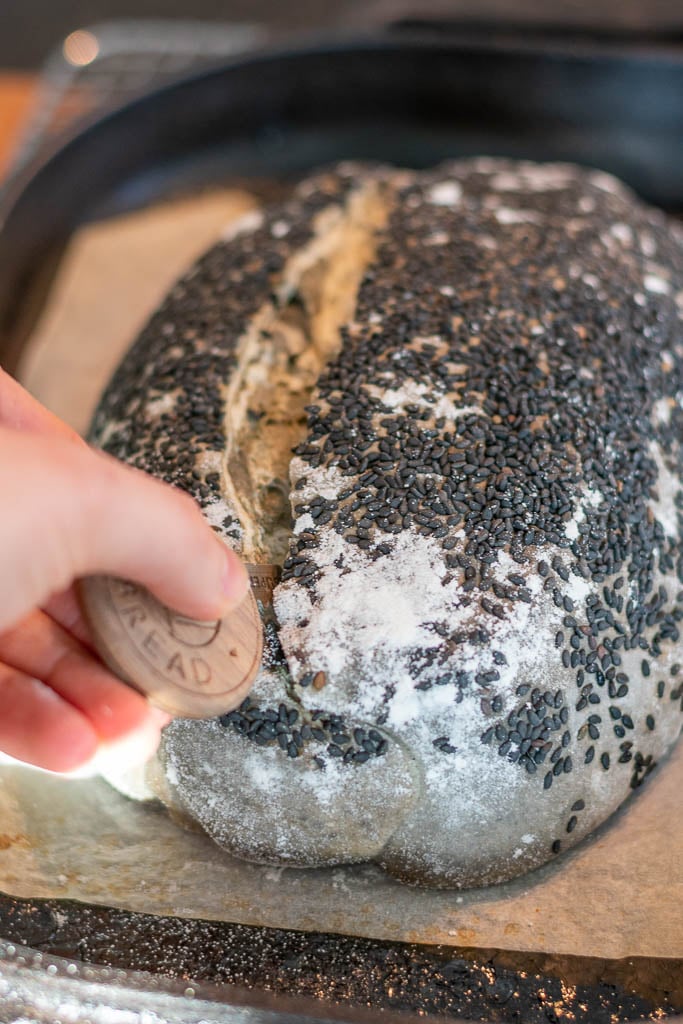 Hand scoring black sesame sourdough bread with a bread lame