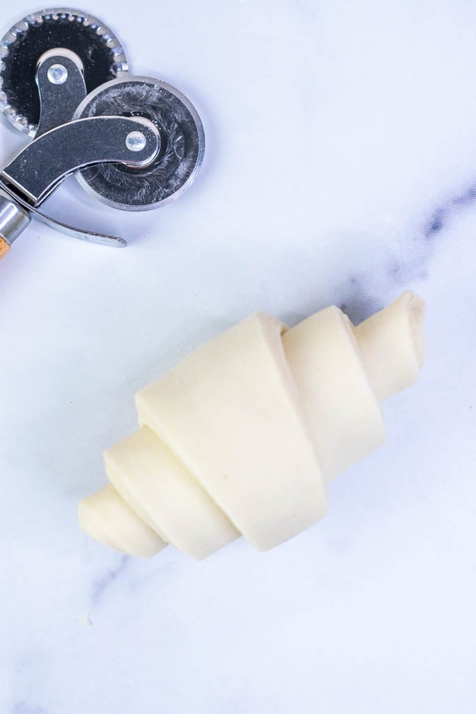 A shaped croissant and pastry wheel on a marble surface