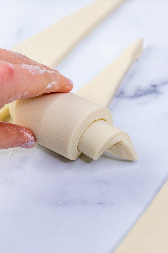 Hand rolling up croissants on a marble surface