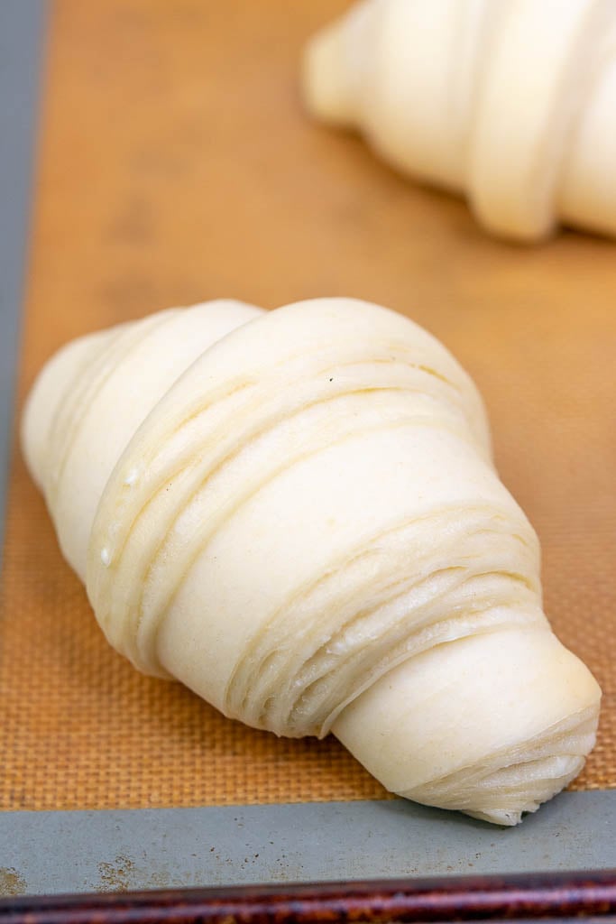 A puffy and proofed sourdough croissant with visible layers on a baking sheet at the end of proofing