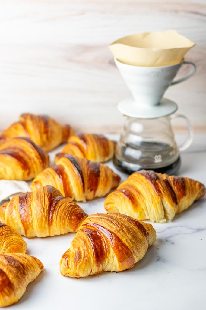 Multiple sourdough croissants on a marble surface with a pourover coffee in background