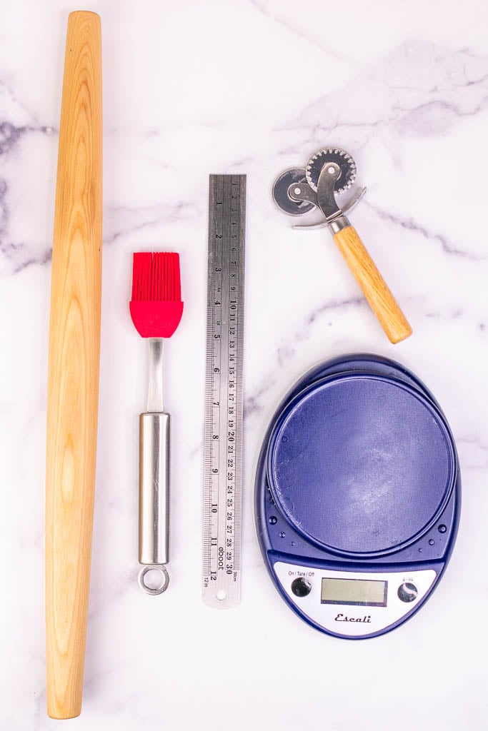 Tools needed for sourdough croissants including a rolling pin, ruler, pastry cutter, pastry brush, and baking scale