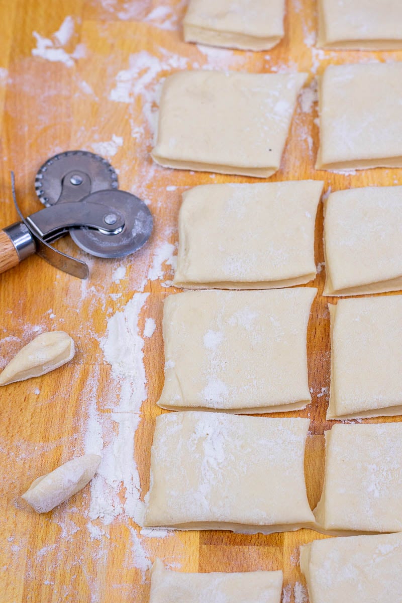 Small squares of beignets are cut with a pastry wheel on a floured surface.
