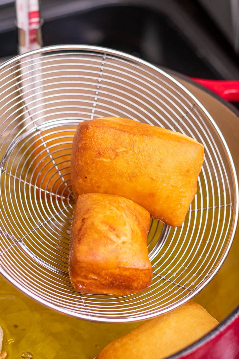 Spider strainer scooping up two beignets from oil.