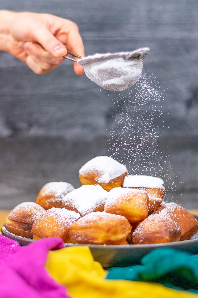 Dusting sourdough beignets with powdered sugar