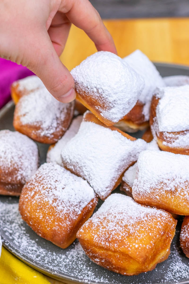 Hand picking up a sourdough beignet dusted with powdered sugar