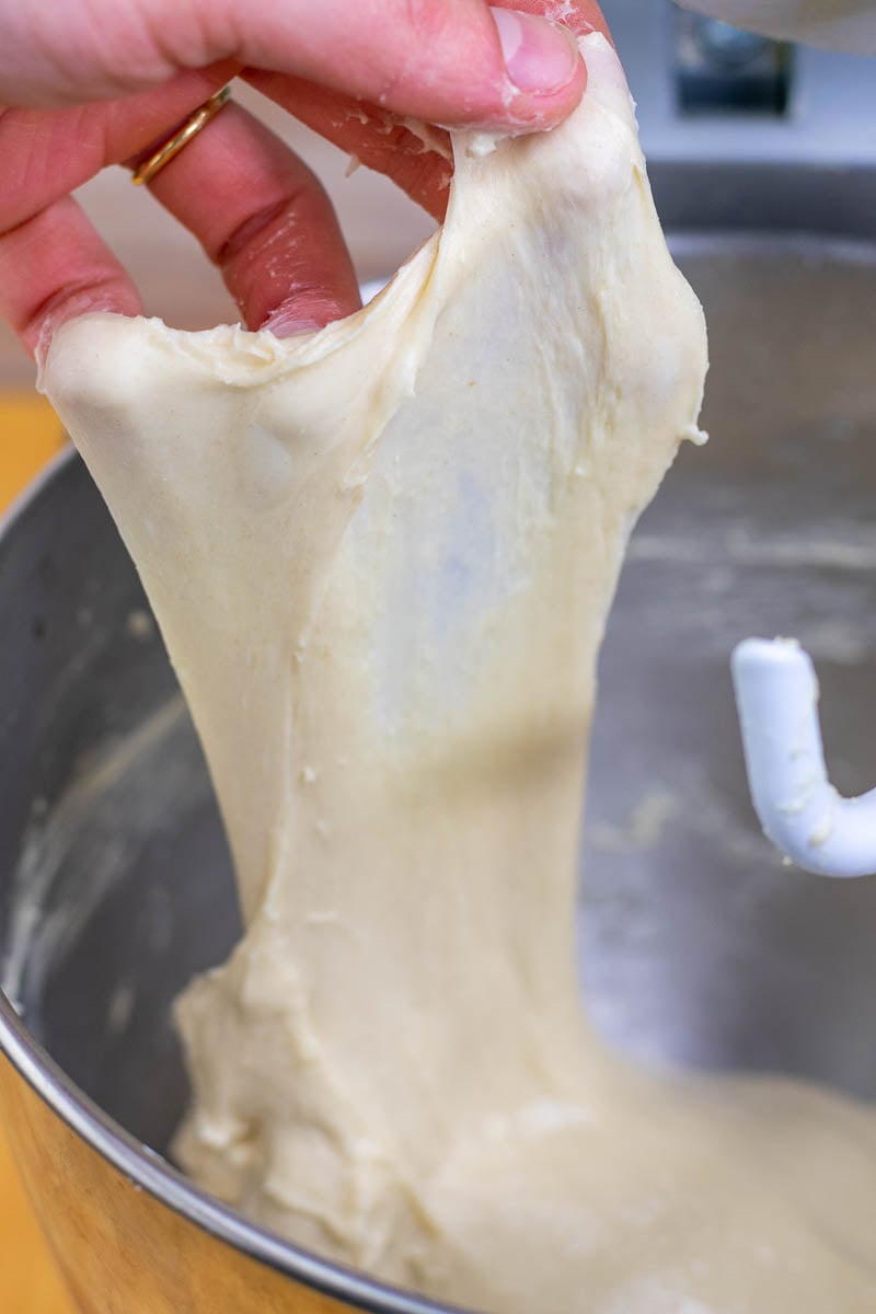 Hand pulling a piece of beignet dough to pass the windowpane test.