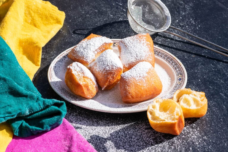 Sourdough beignets dusted with powdered sugar on a plate with Mardi Gras colors