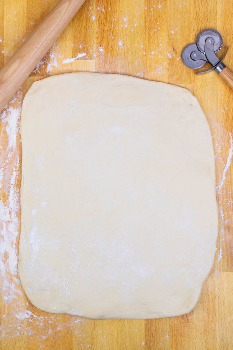 Beignet dough rolled out on counter into a large rectangle with a rolling pin and pastry cutter