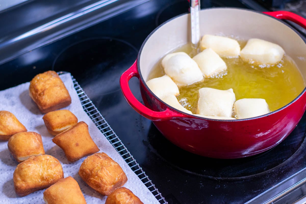 Set-up for frying beignets including a dutch oven with oil and a cooling rack with paper towel with beignets on it.