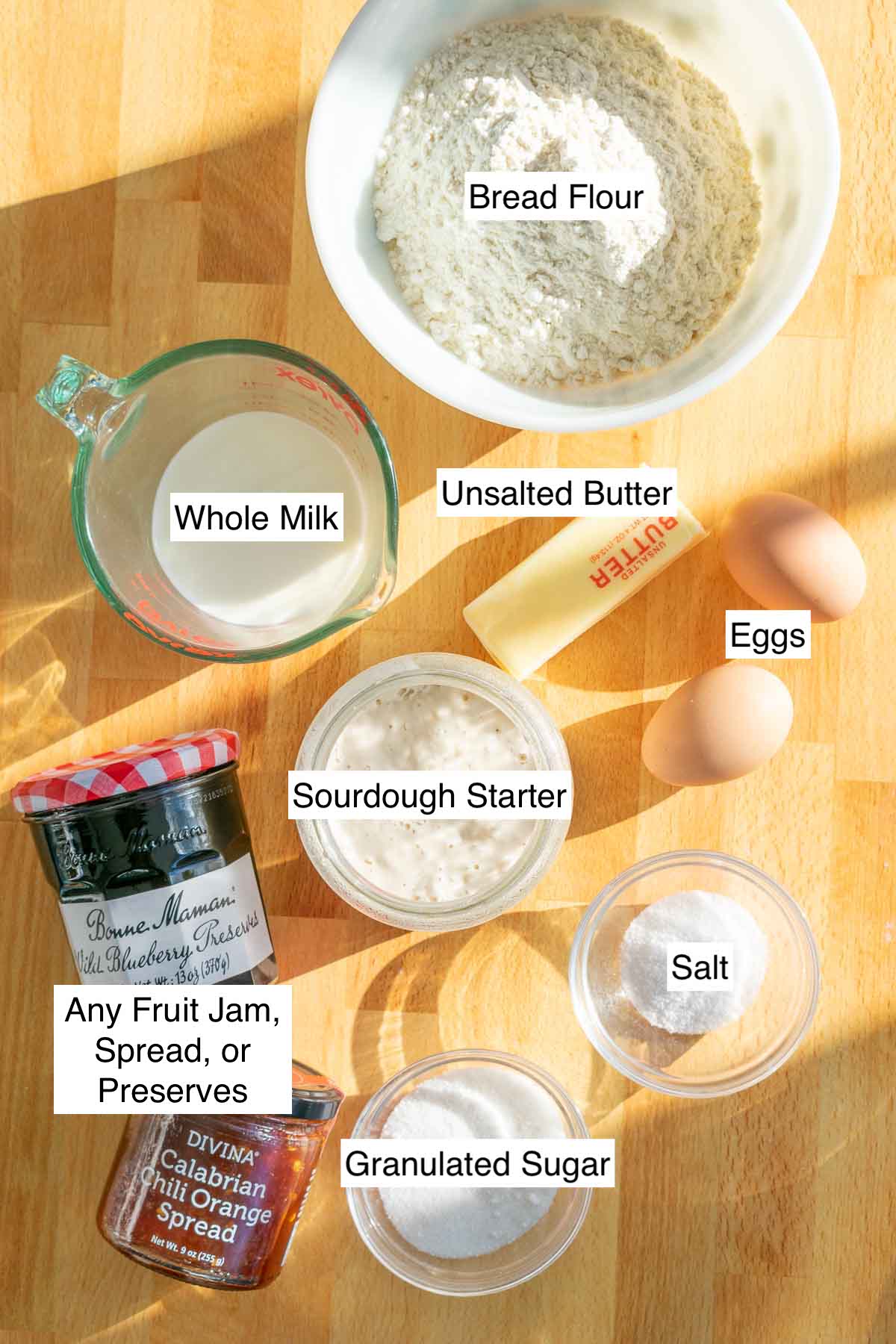 Labeled ingredients needed for Sourdough babka including bread flour, whole milk, eggs, unsalted butter, sourdough starter, sugar, salt, and any jam