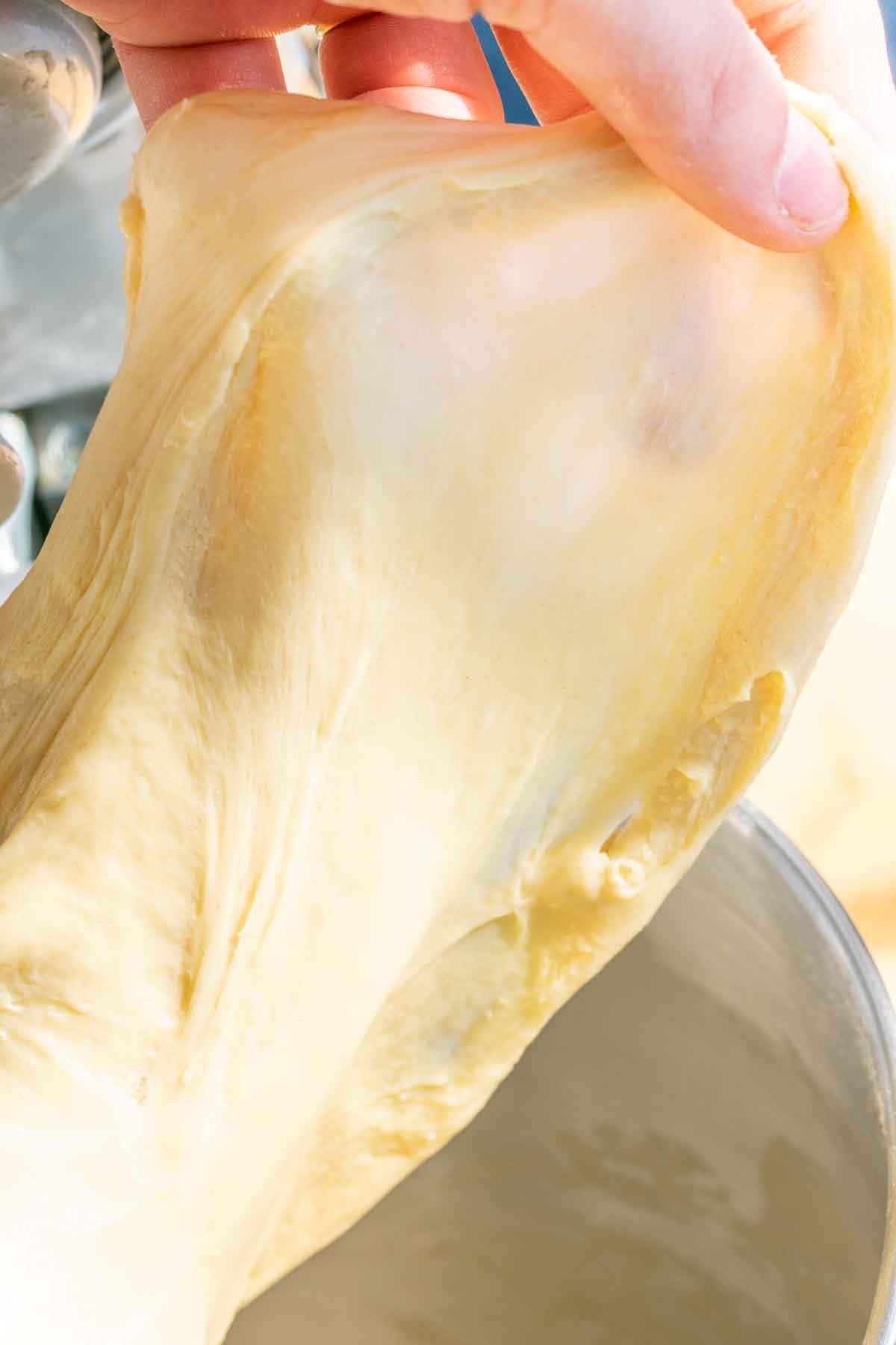 Hand pulling a piece of babka dough for the windowpane test