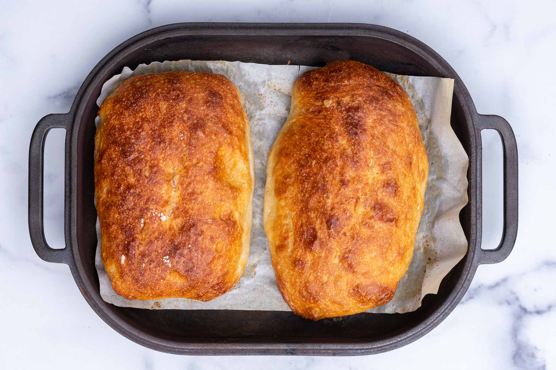Two baked sourdough pan de cristal breads in a challenger bread pan