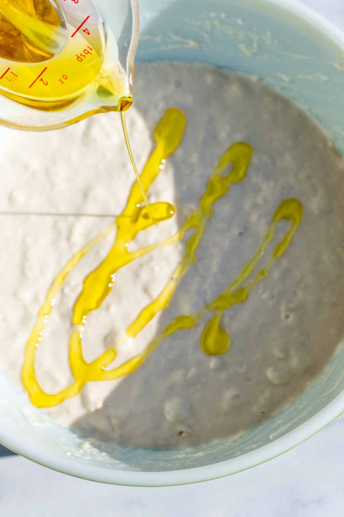 Drizzling olive oil into bowl of dough