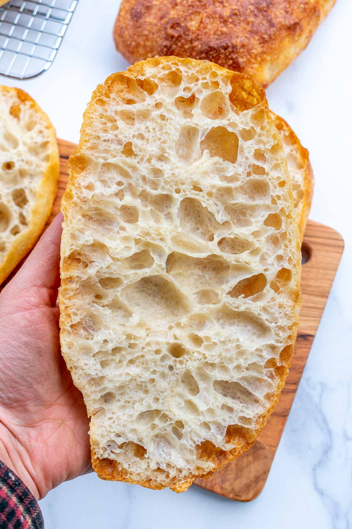 Hand holding a slice of sourdough pan de cristal with a holey interior