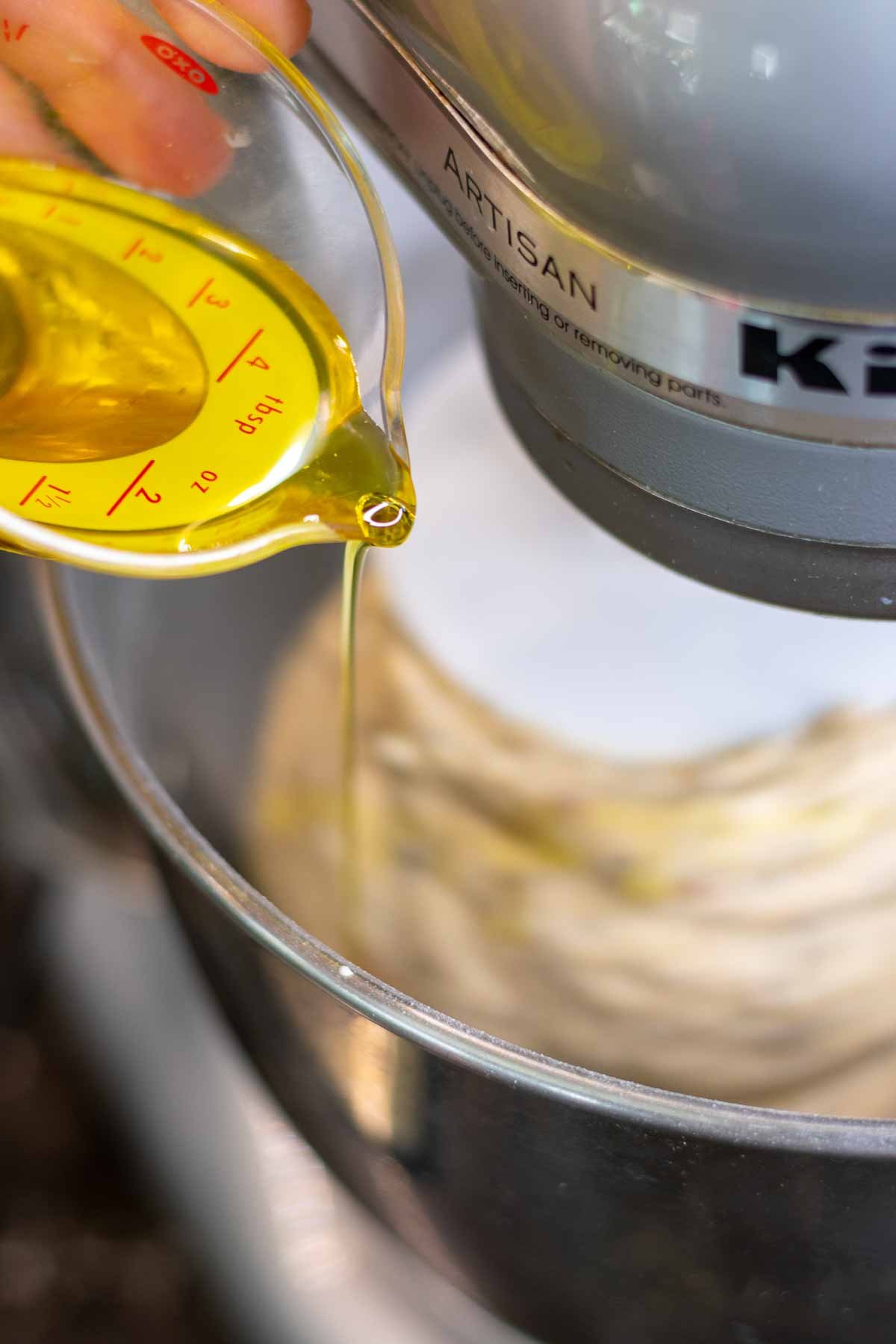 Slowing pouring in olive oil in bowl of stand mixer