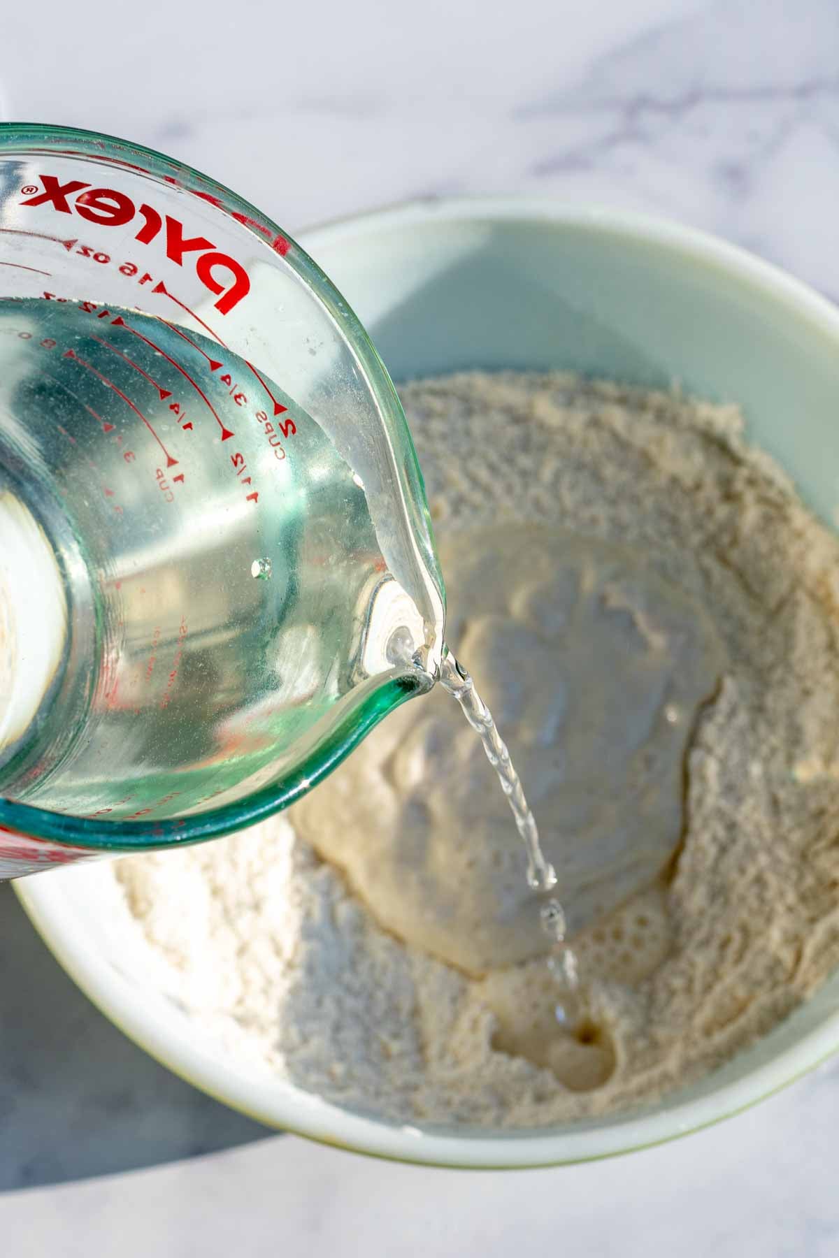 Pouring water into a bowl of flour and sourdough starter