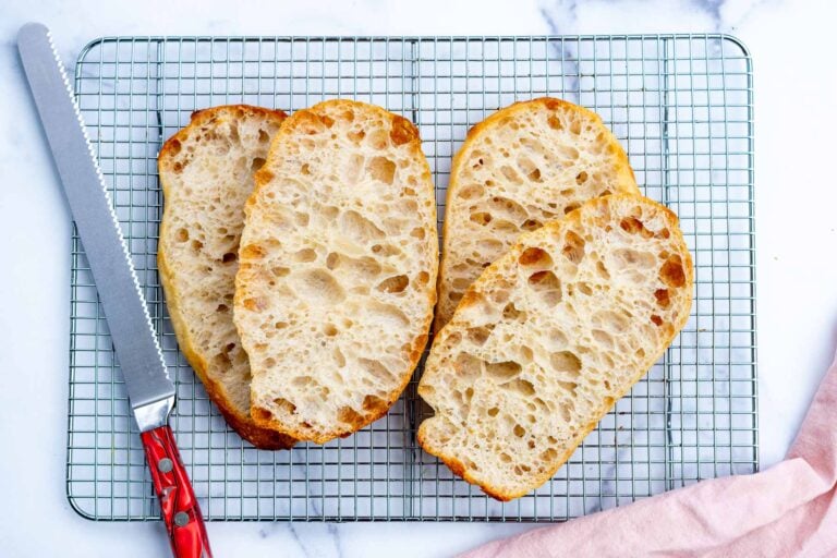 Four slices of sourdough pan de cristal on a wire rack with a bread knife