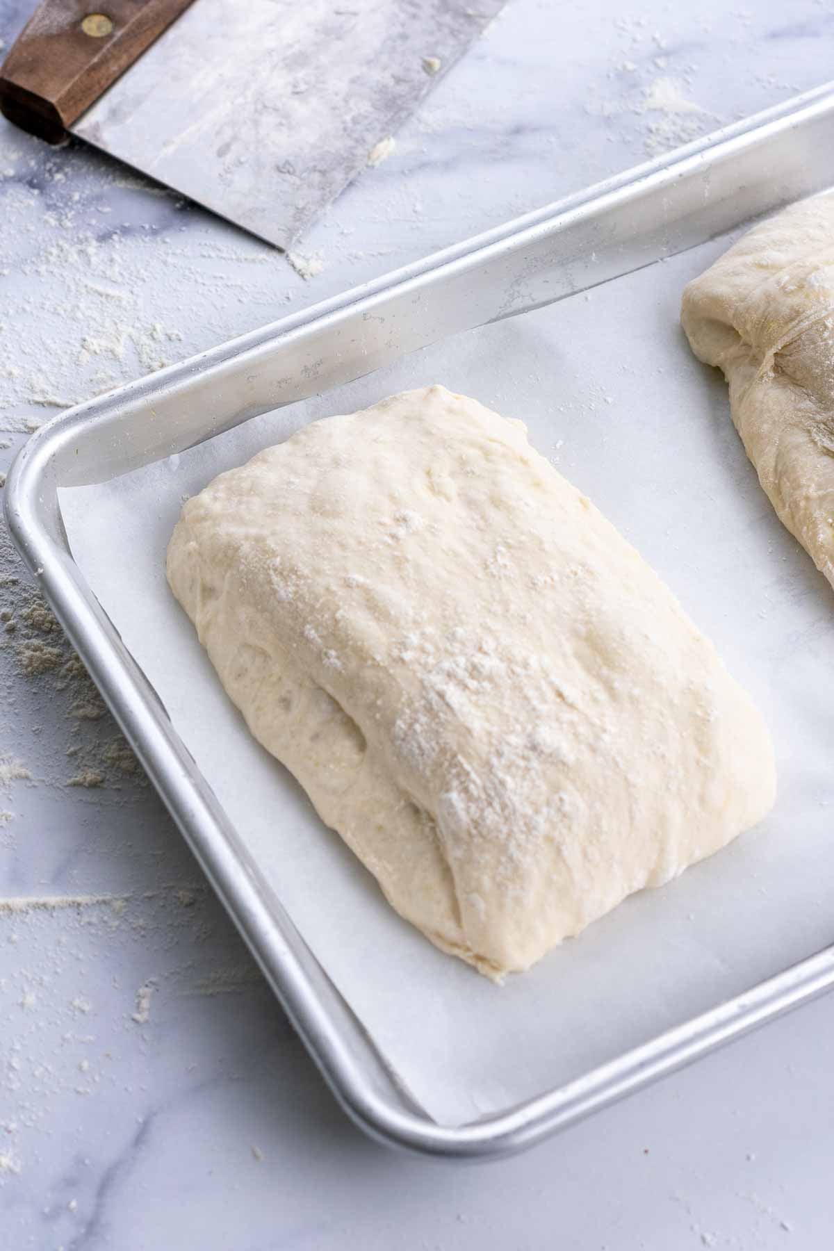 Unbaked pan de cristal dough on a quarter sheet pan on parchment paper