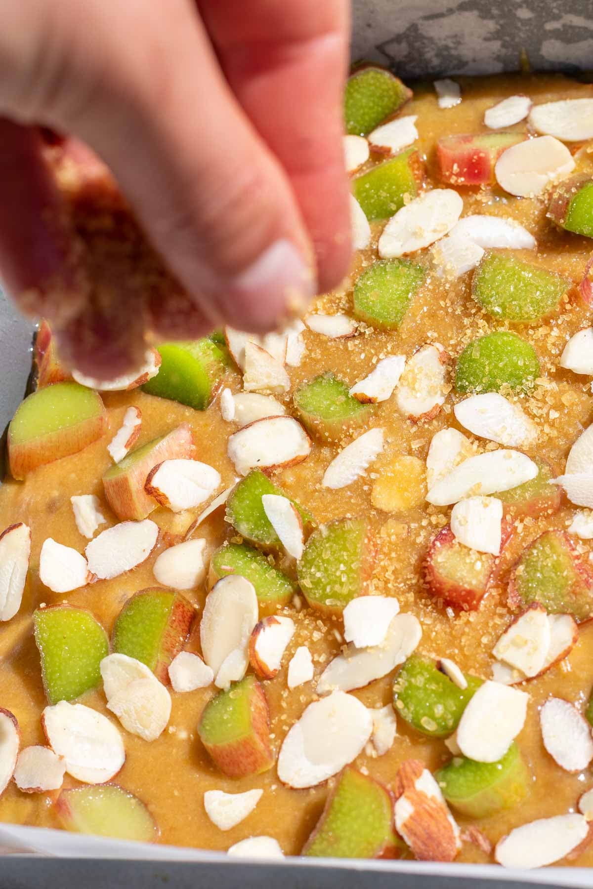 Sprinkling raw sugar on top of sourdough blondies with rhubarb and almonds