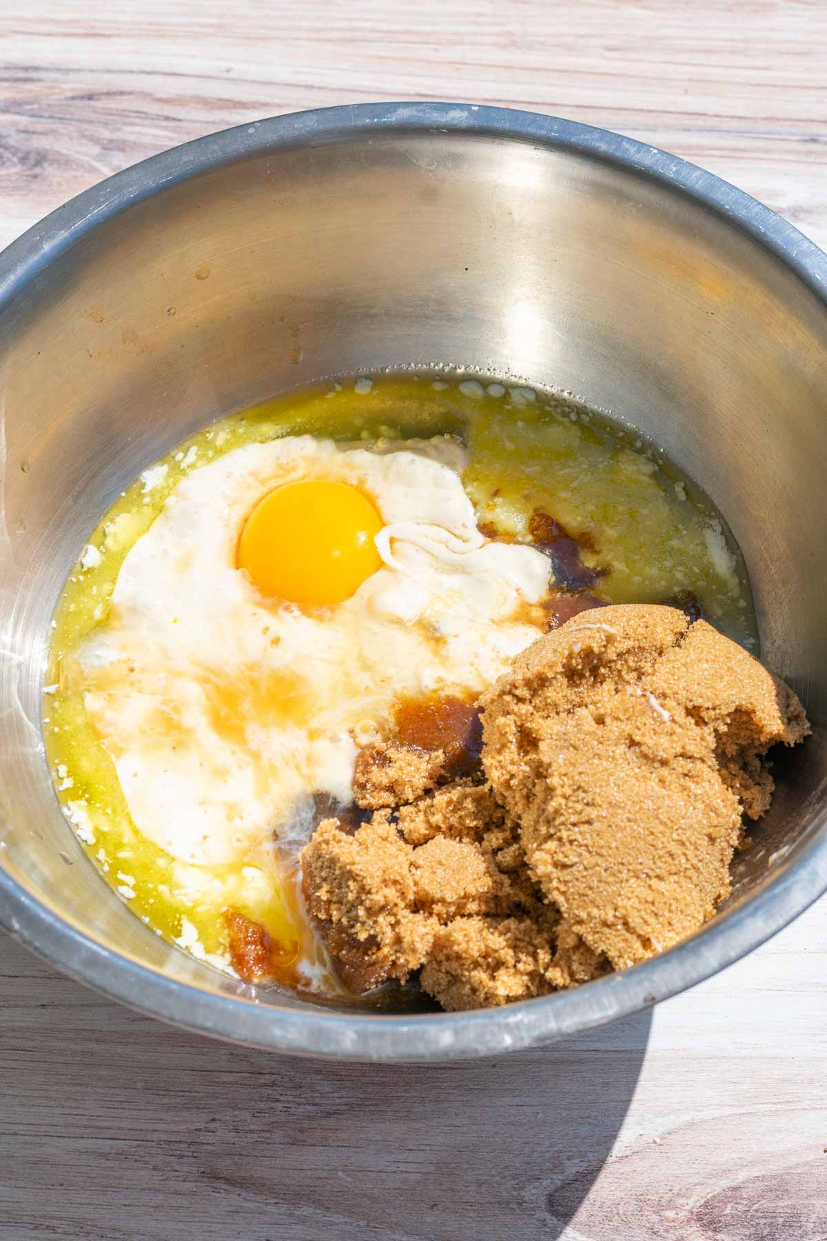 wet ingredients in mixing bowl including butter, brown sugar, an egg, vanilla extract, and almond extract