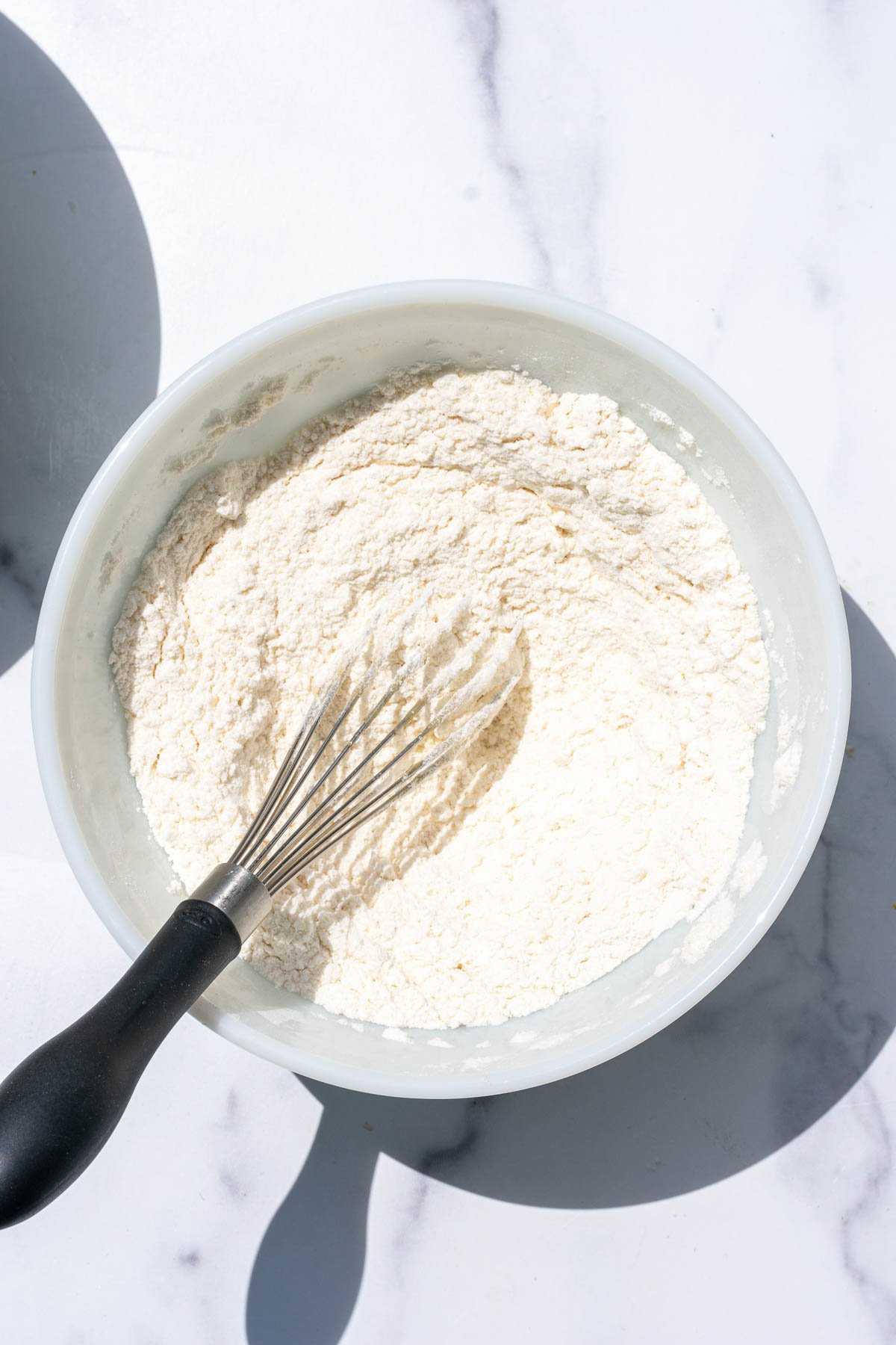 Flour, salt, baking soda, and baking powder mixed together in bowl with a whisk
