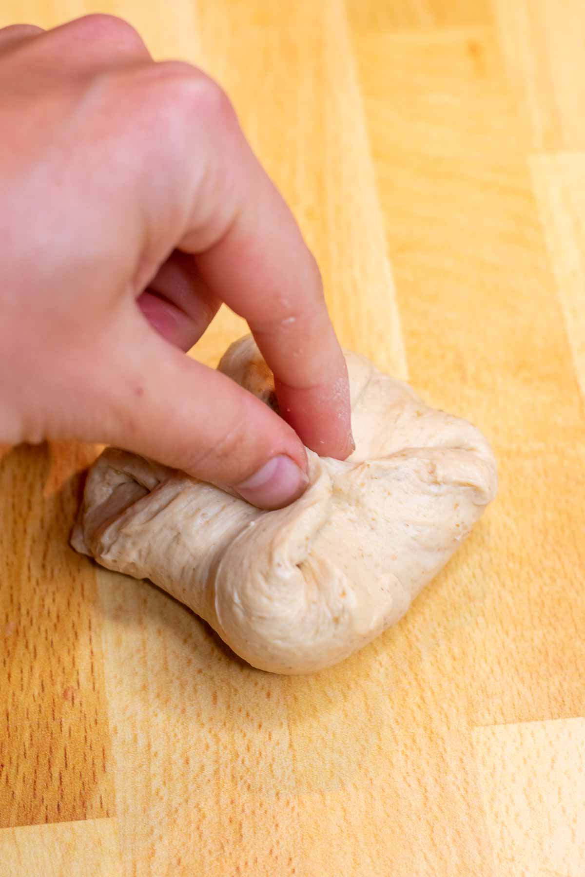 Pinching the corners of bagel dough together into a package