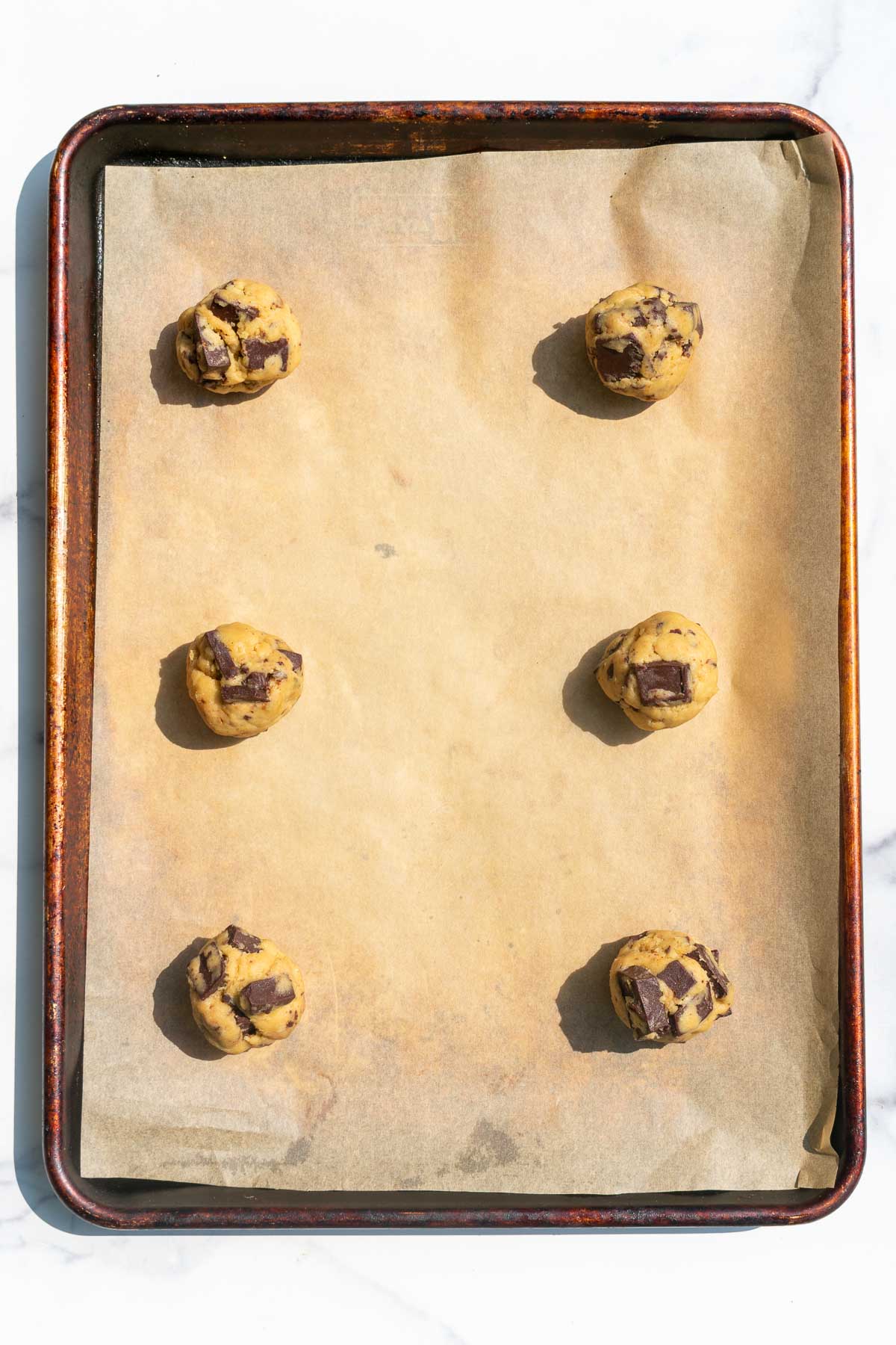 Six sourdough discard chocolate chip cookie balls on a parchment lined baking sheet.