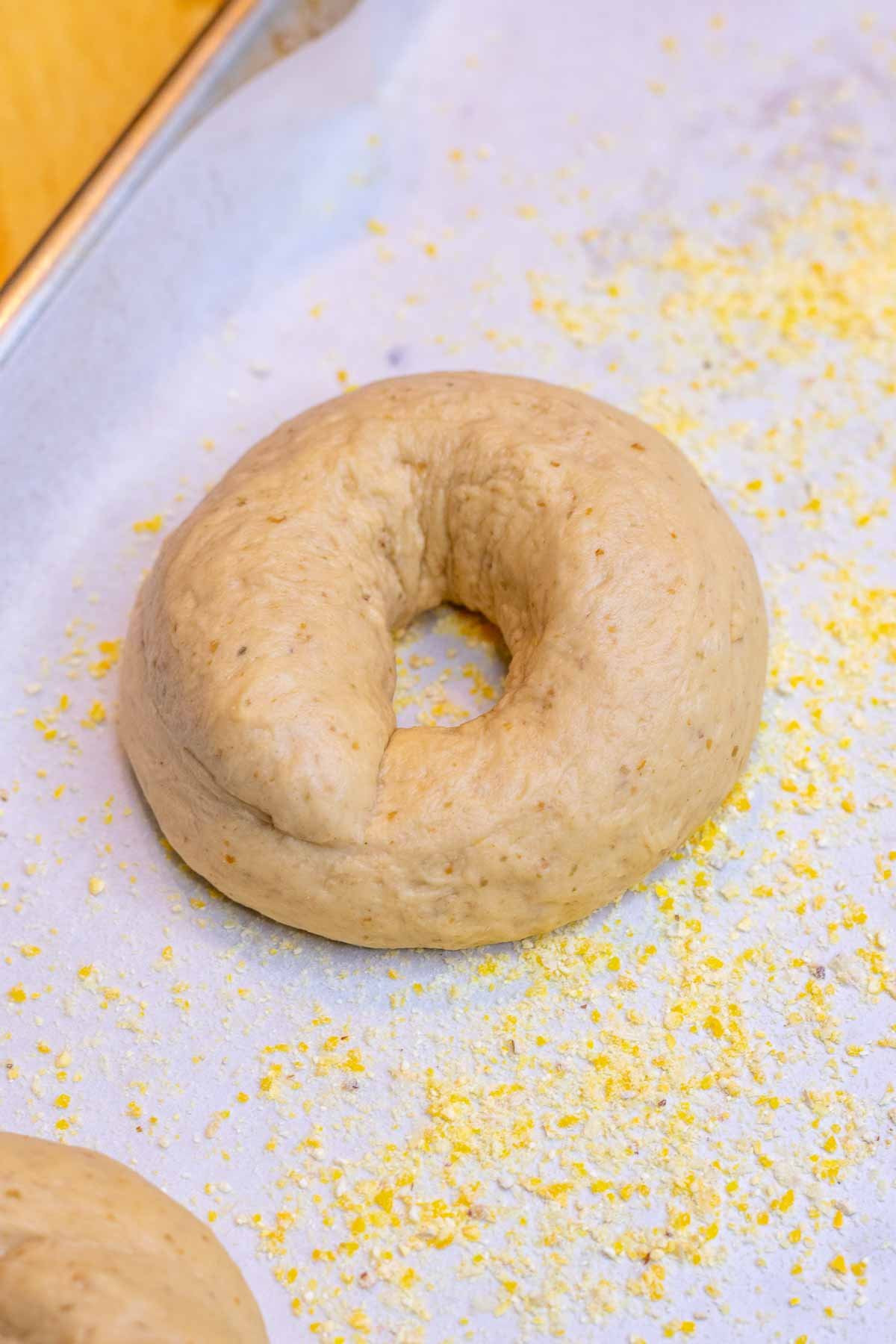 A sourdough bagel on a prepared baking sheet dusted with cornmeal