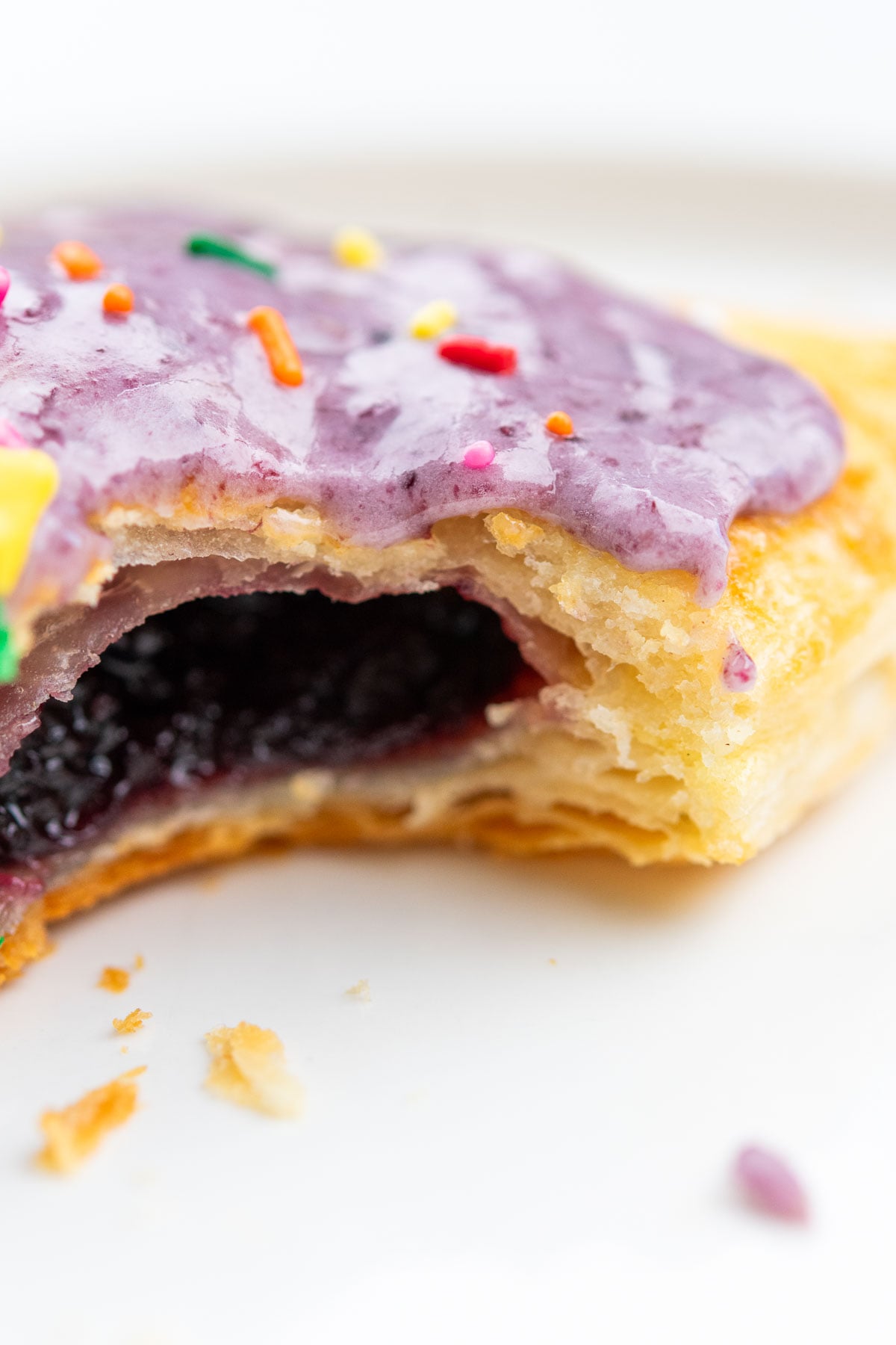 Close up of a bite taken from a blueberry sourdough pop tart made with sourdough rough puff pastry with many flaky layers visible.