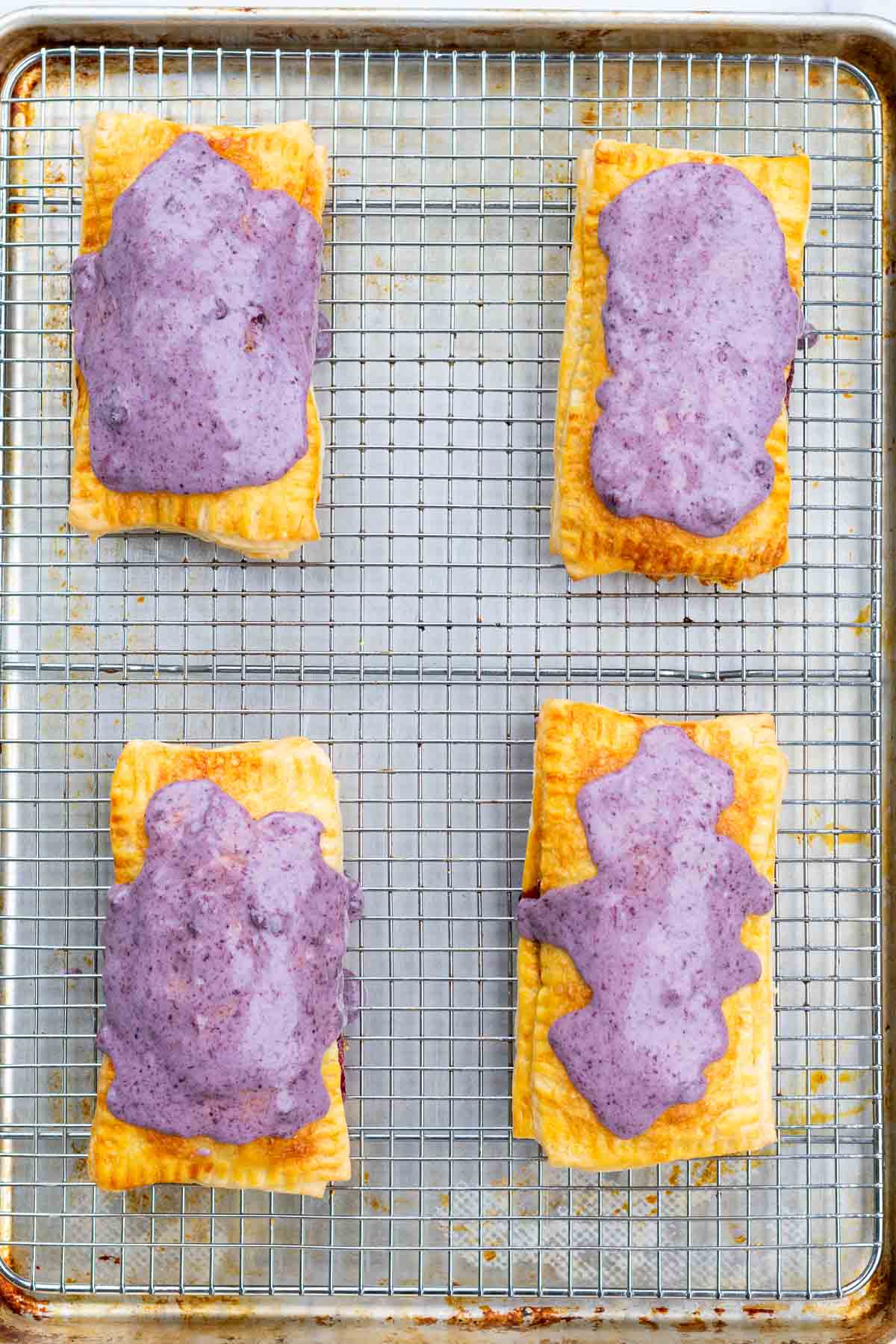 Four sourdough pop tarts on a wire rack with blueberry icing on top.