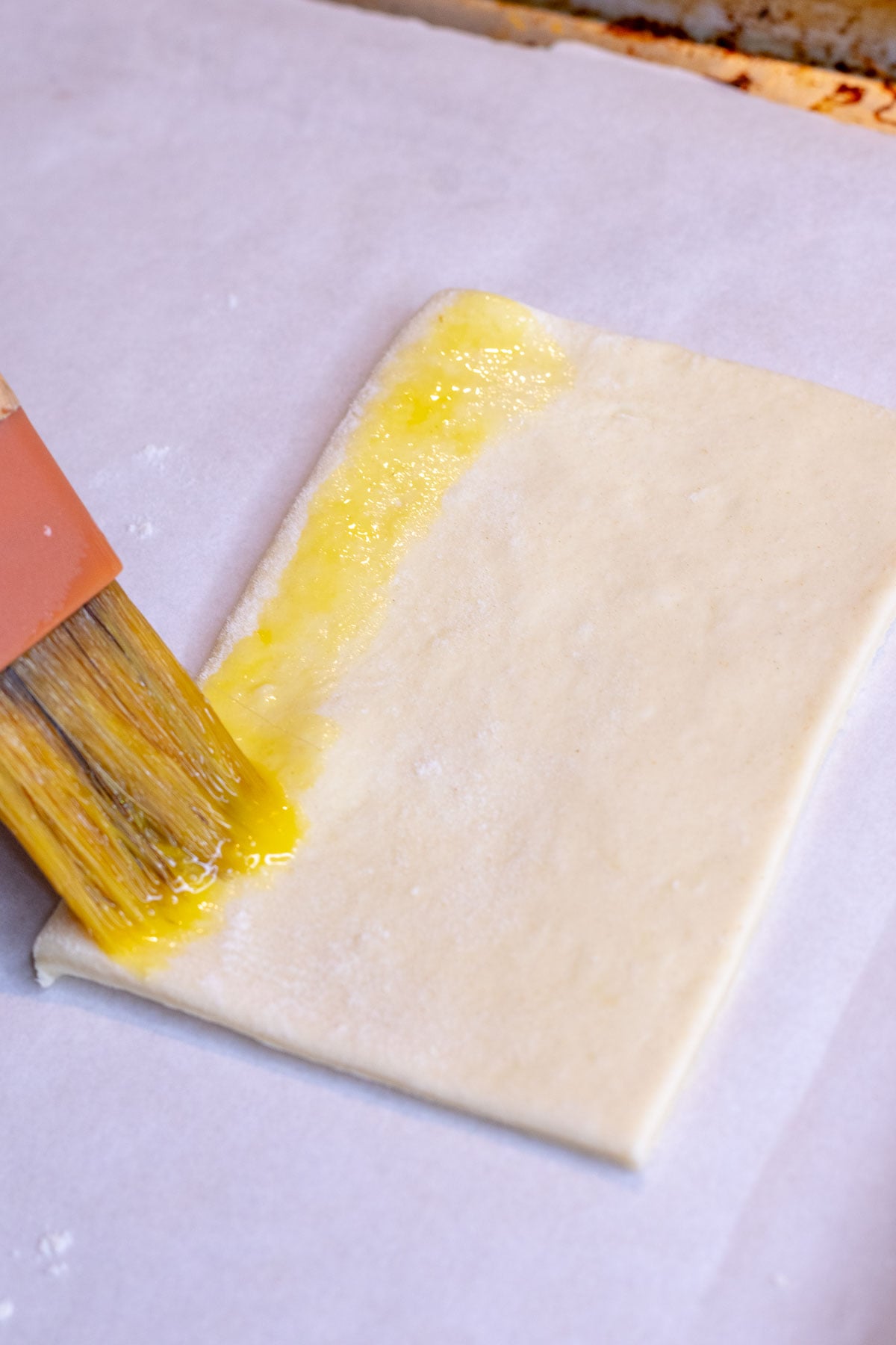 Pastry brush brushing the edges of puff pastry with egg wash