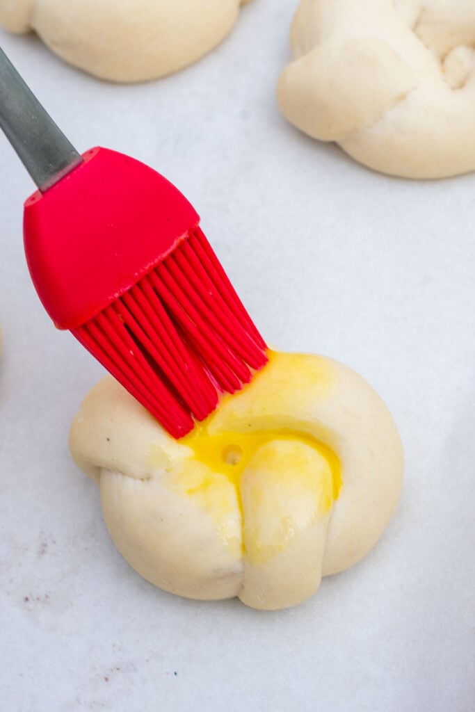 Brushing an egg wash on a sourdough garlic knot before baking
