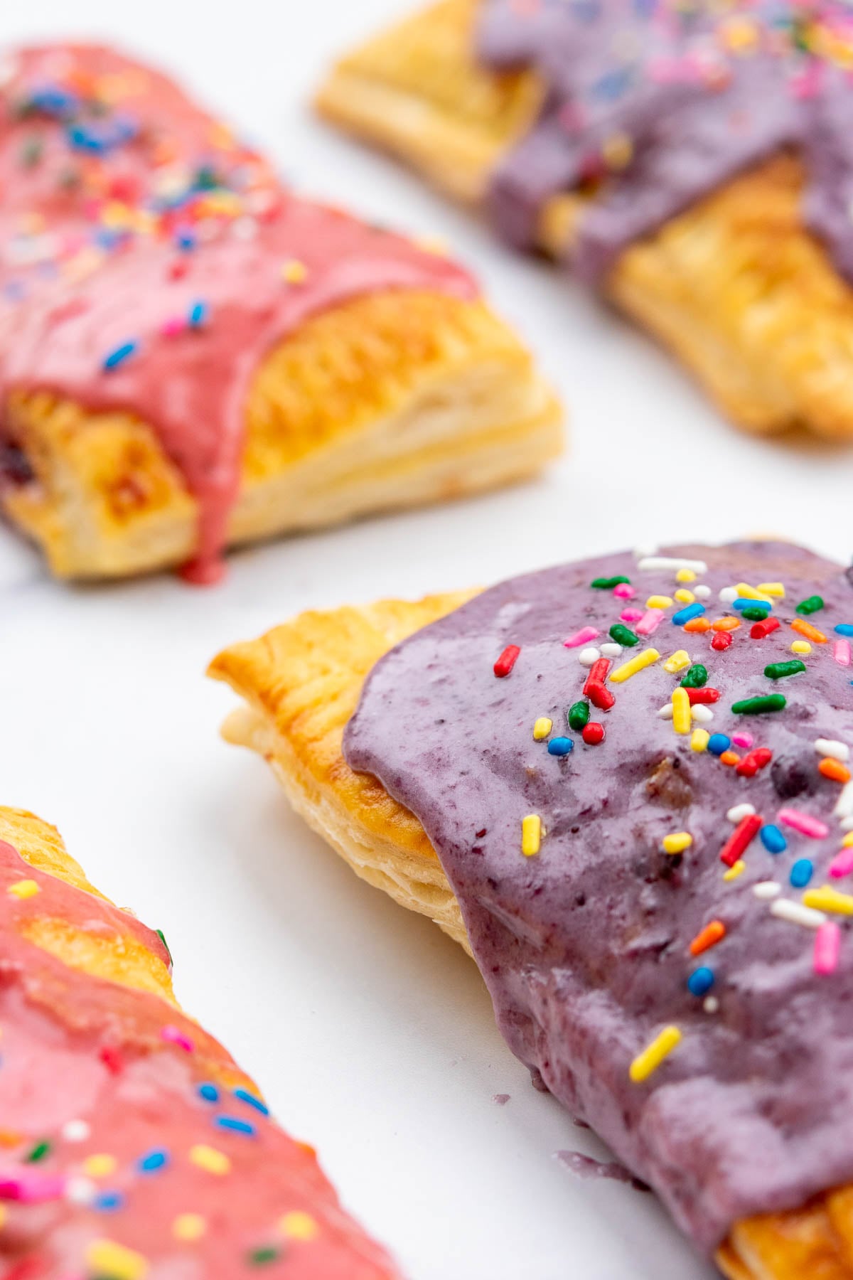 Close up of flaky sourdough pop tarts made with sourdough rough puff pastry and topped with blueberry and strawberry jams and rainbow spprinkles