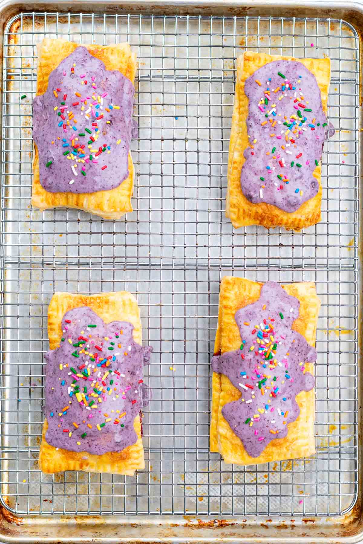 Four sourdough pop tarts on a wire rack with blueberry jam icing and rainbow sprinkles