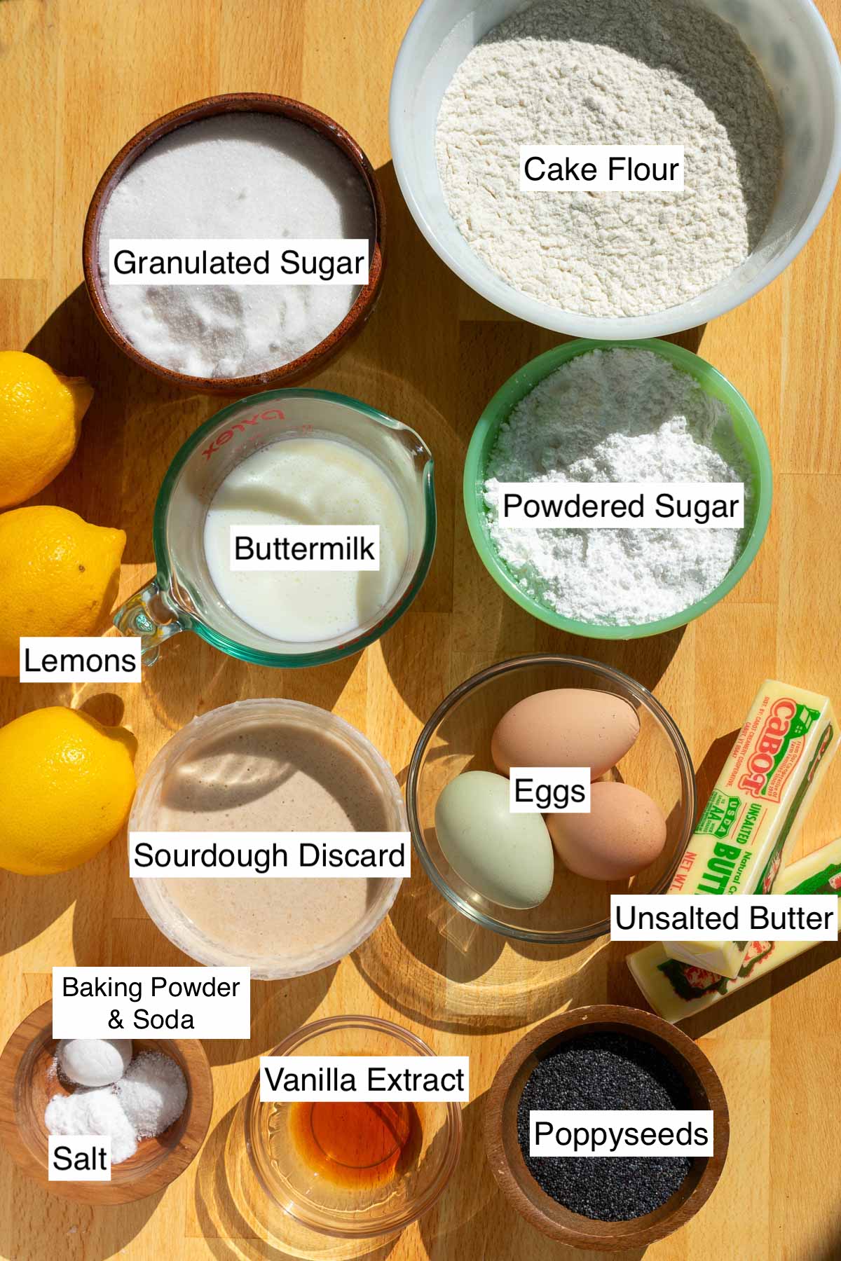 Ingredients needed for sourdough lemon poppy seed bundt cake including cake flour, sugar, salt, baking powder, baking soda, butter, eggs, vanilla, poppy seeds, lemons, buttermilk, and sourdough discard