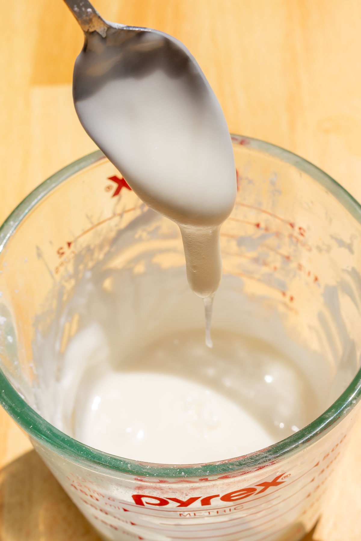 Spoon lifting lemon sugar glaze in liquid measuring cup