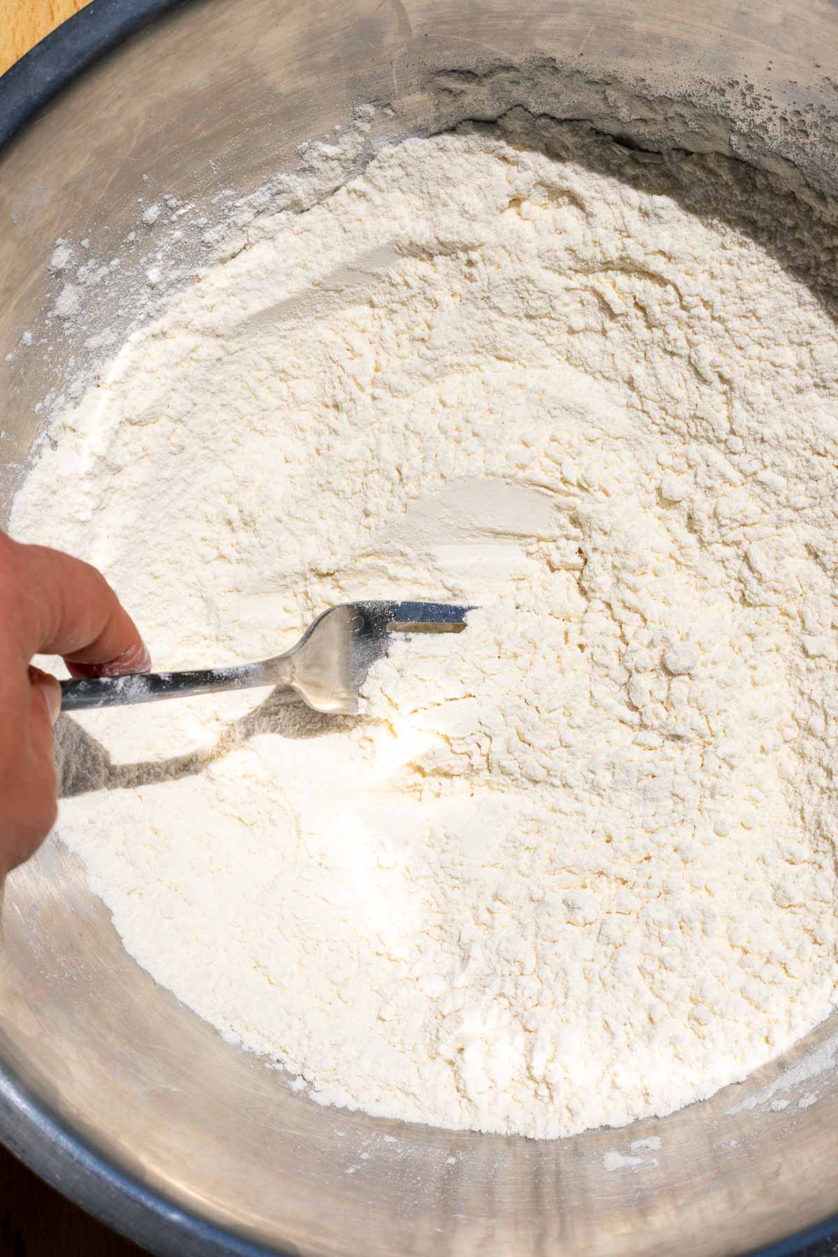 Fork mixing flour and salt in a mixing bowl