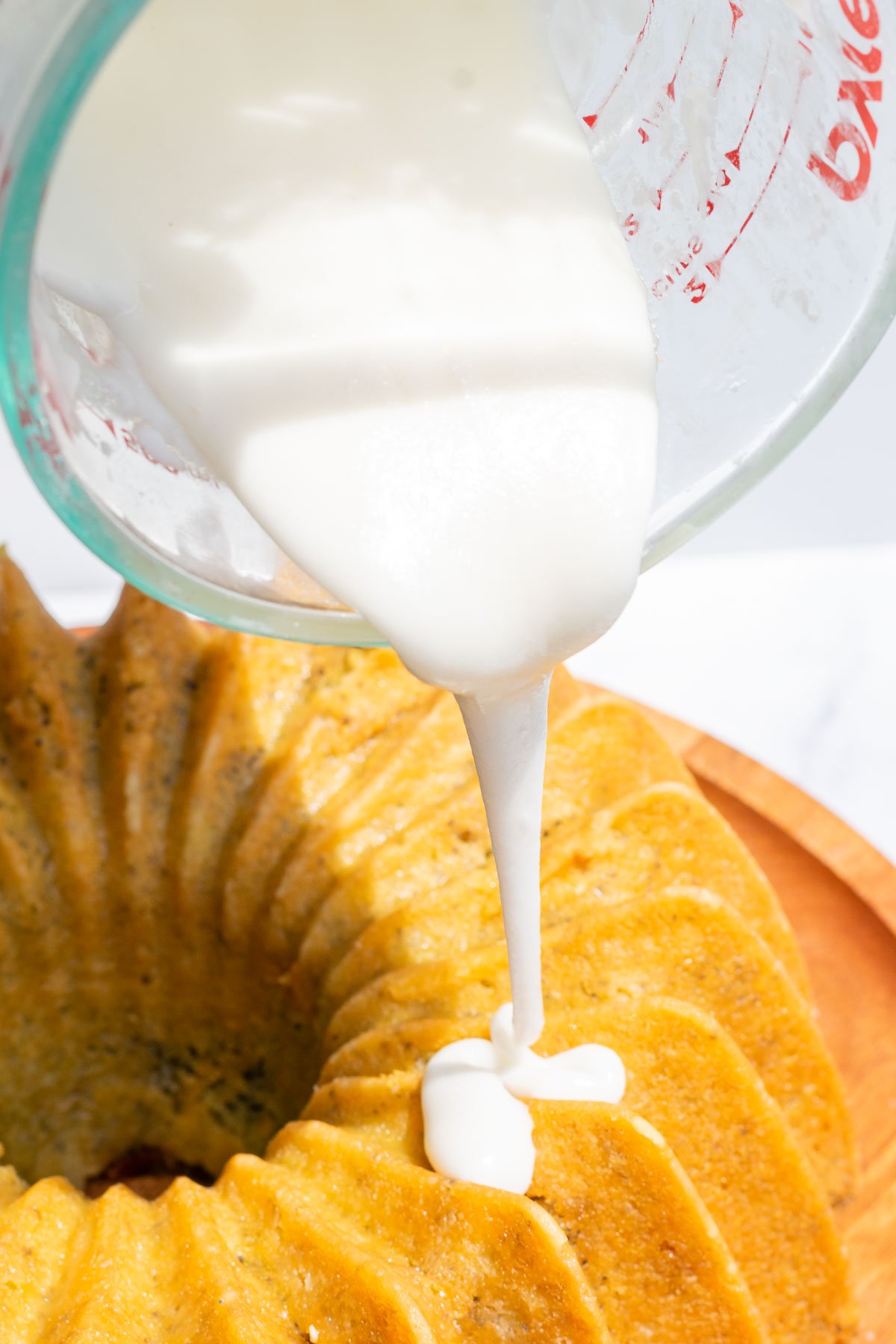 Liquid measuring cup pouring lemon glaze on top of bundt cake