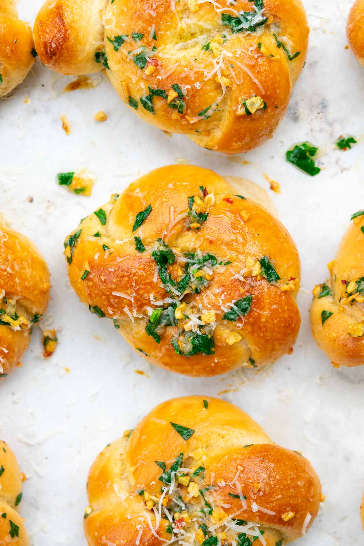 Baked sourdough garlic knots on parchment paper, brushed with garlic butter, parmesan, and parsley