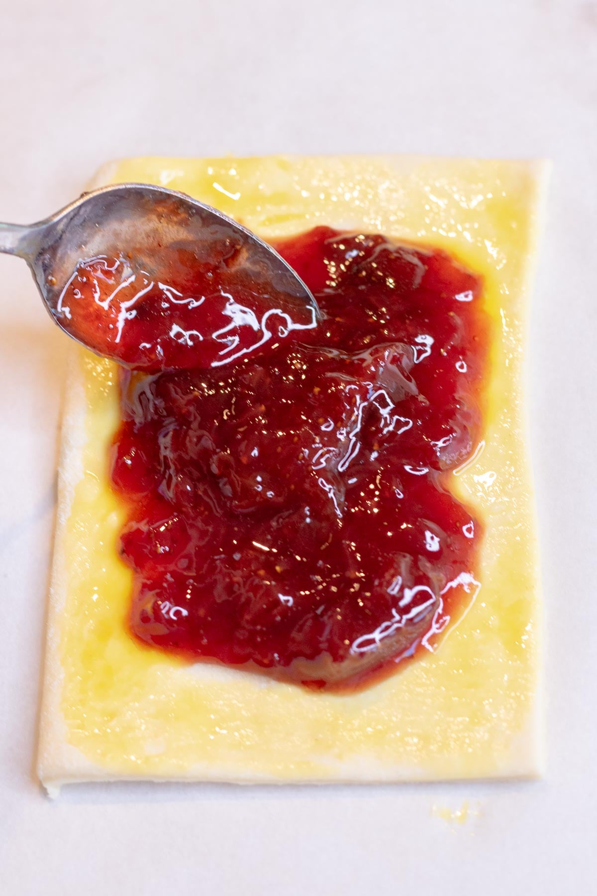 Spooning strawberry jam on top of a sourdough pop tart.