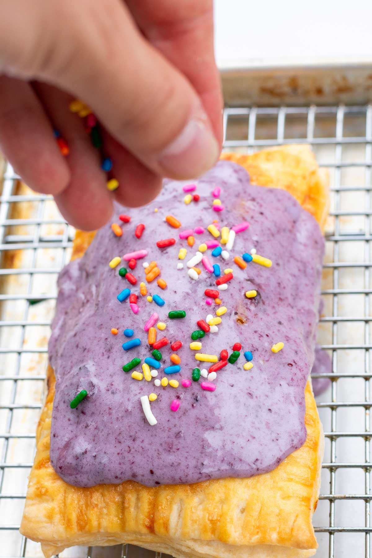 Sprinkling rainbow sprinkles on top of a sourdough pop tart