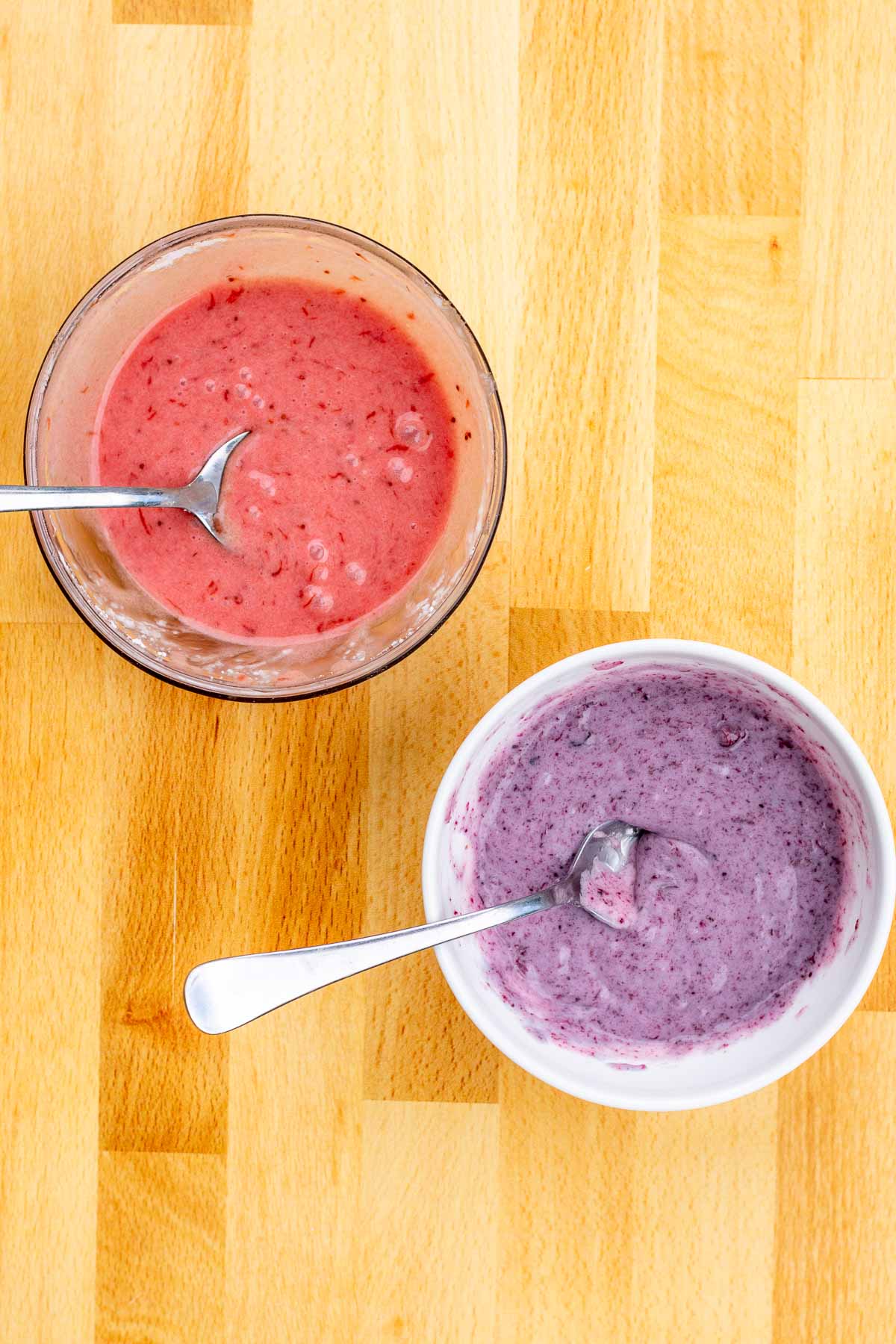 Two bowls of strawberry and blueberry icing with spoons in them.