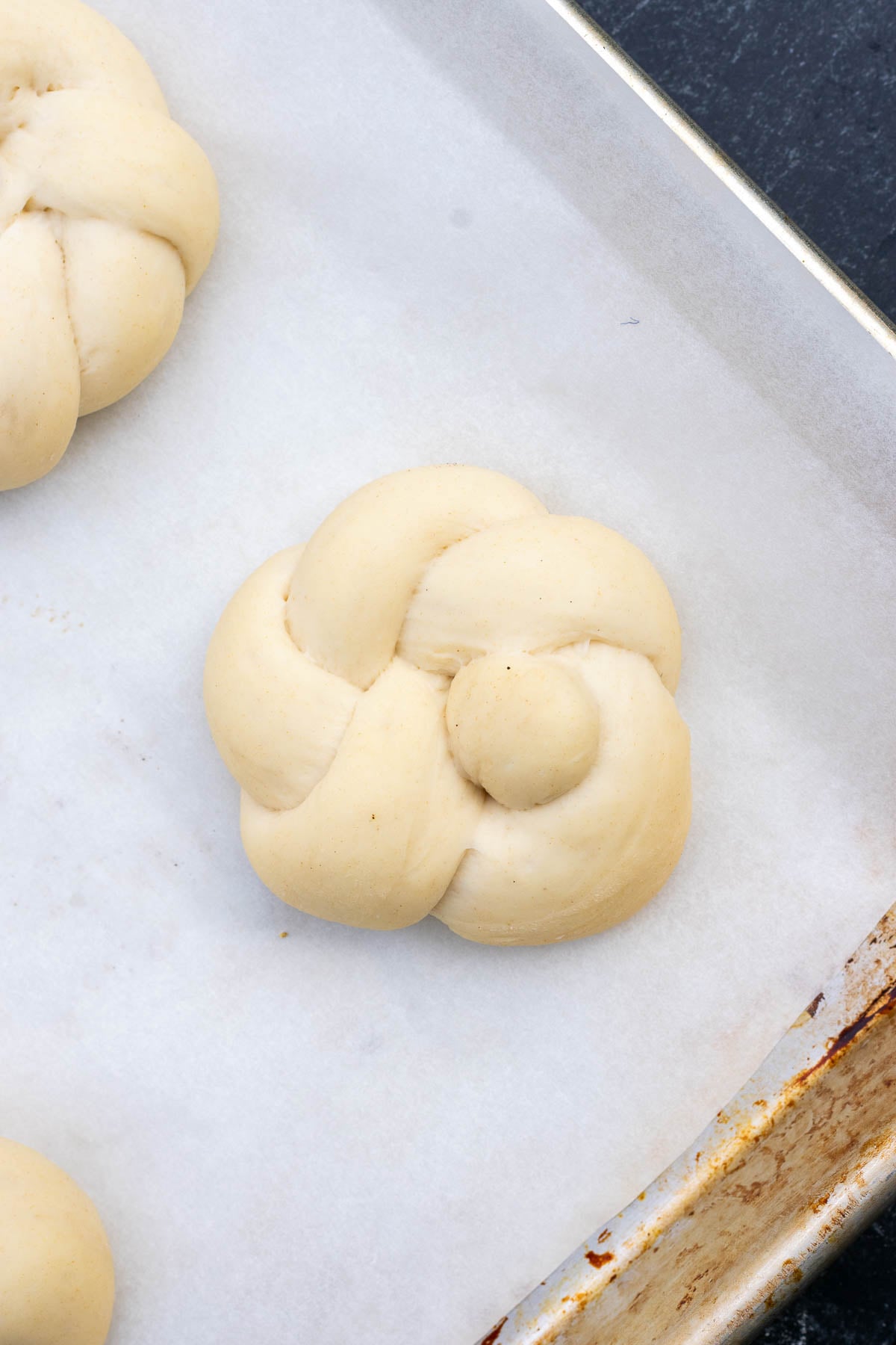 A poofy sourdough garlic knot on a baking sheet at the end of proofing.