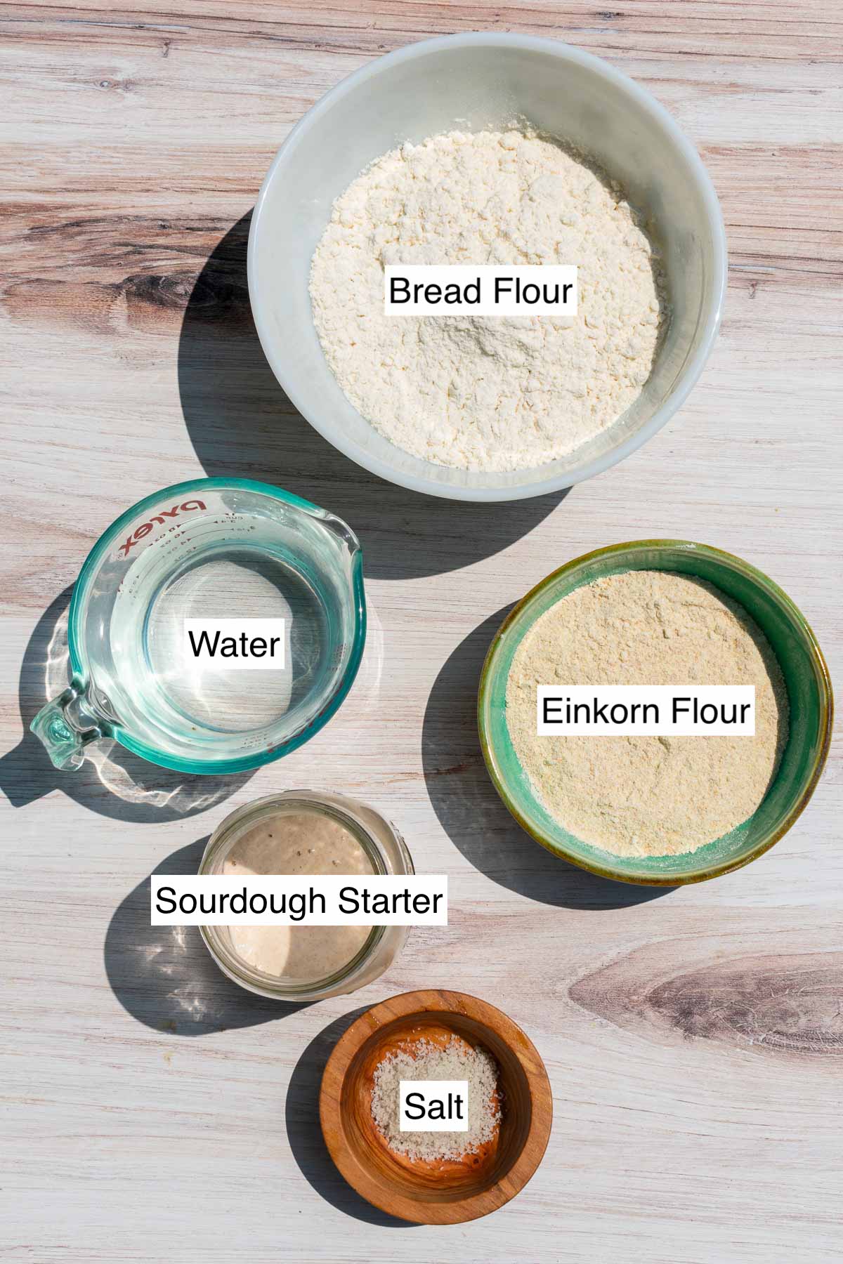 Labeled bowl of ingredients needed for beginner's einkorn sourdough bread including bread flour, einkorn flour, water, sourdough starter, and salt.