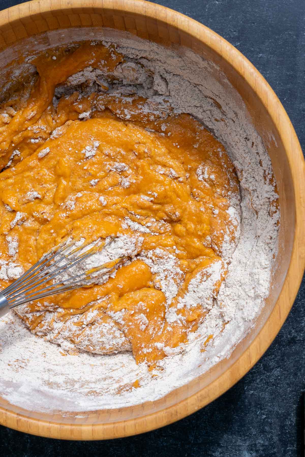 Whisking dry ingredients and wet ingredients for pumpkin muffins together in bowl with a whisk