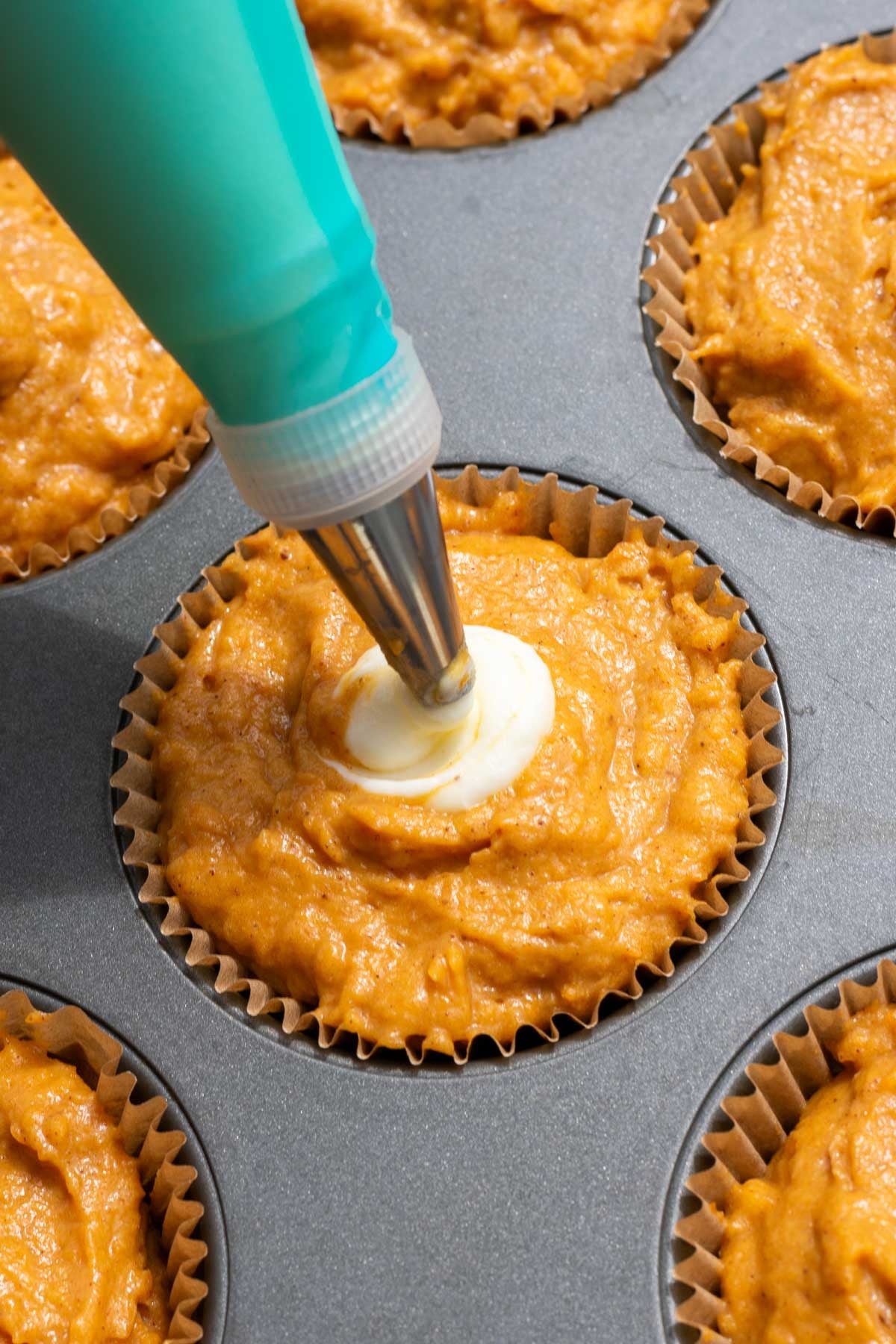 Piping cream cheese filling to the sourdough pumpkin muffin batter