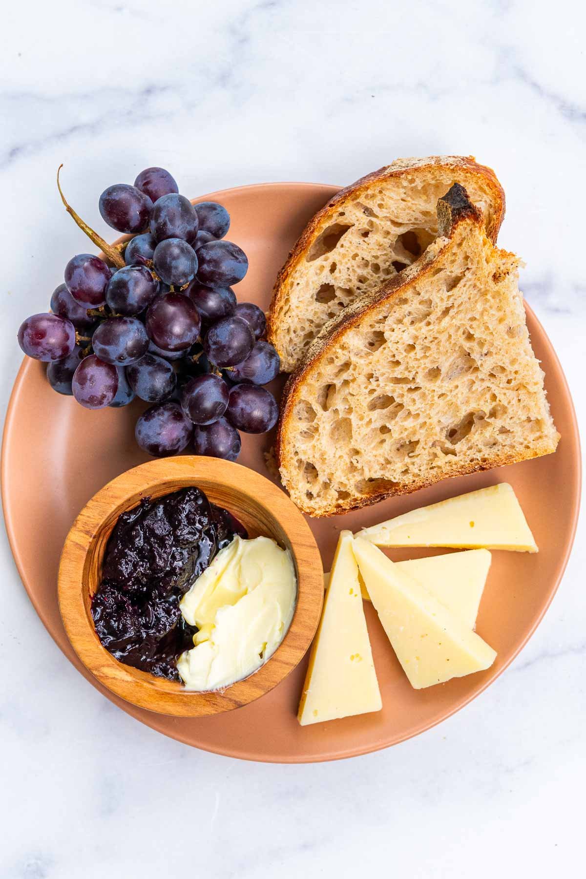 Plate of sourdough bread slices with grapes, cheese, butter, and jam.